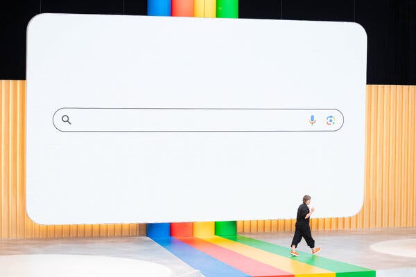 A person walks across a stage where a screen shows a giant version of the Google search bar.